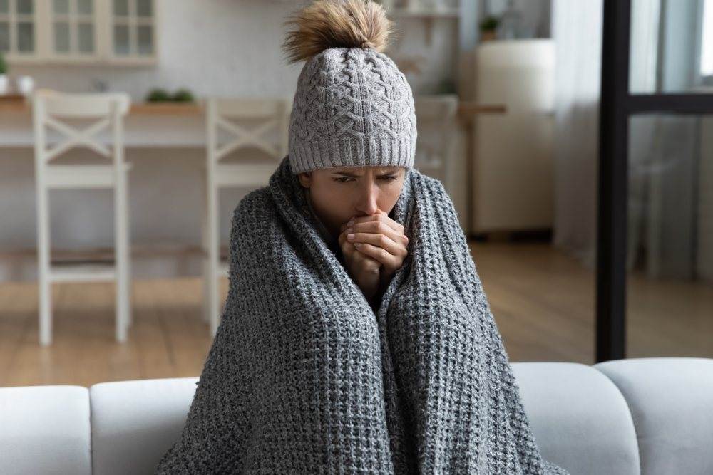 A woman wrapped in a blanket and wearing a hat sits on a couch.